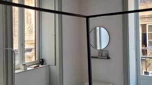 Una stanza con un'ampia finestra, uno specchio, uno scaffale con oggetti decorativi e una panca.