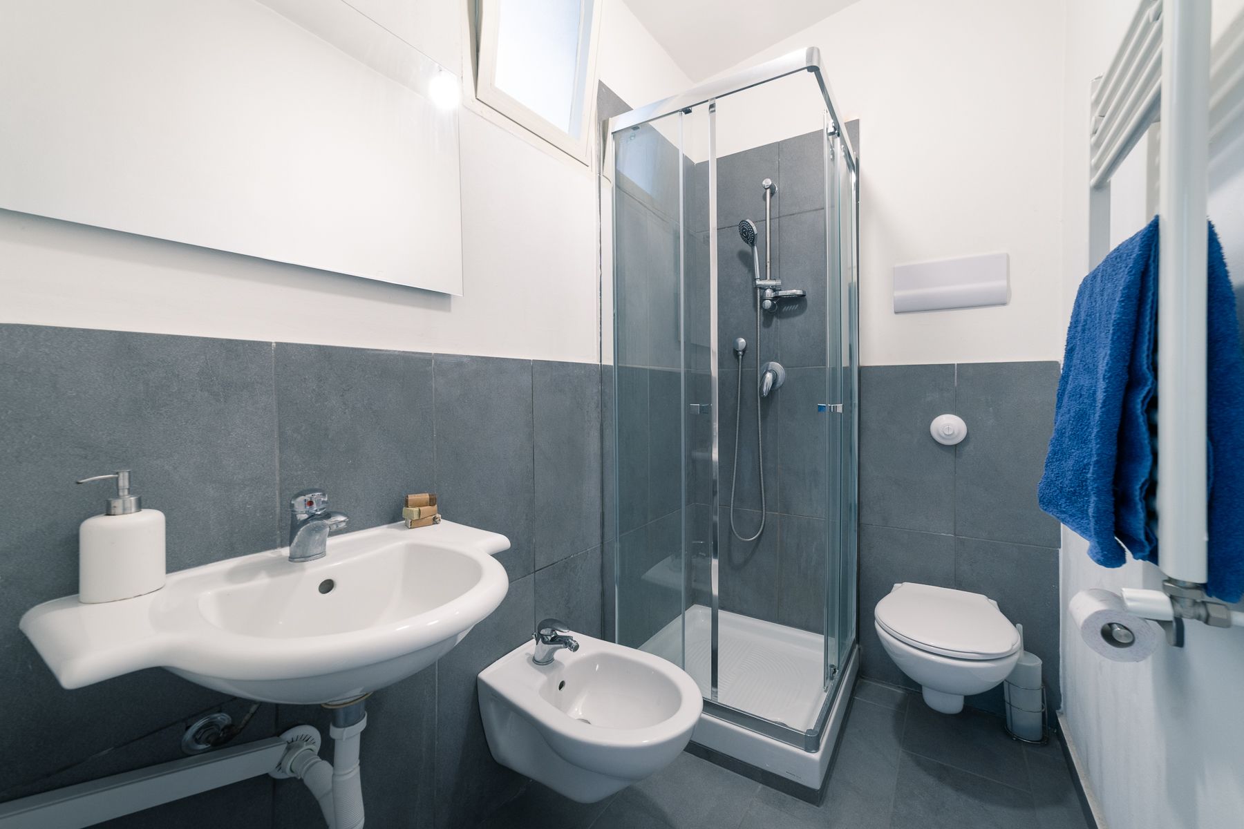 A modern bathroom with a glass-enclosed shower, a pedestal sink, a bidet, and a toilet.