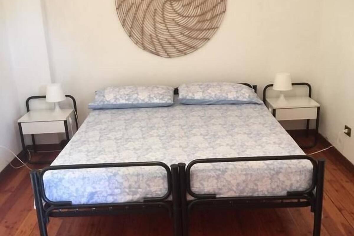 A bed with a patterned mattress, two bedside tables, and a wall-mounted decorative item.