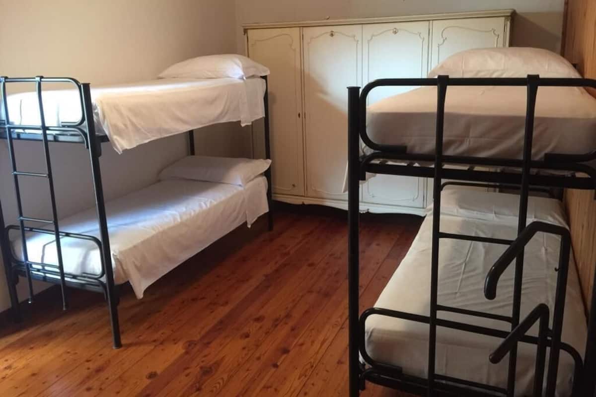 A room with bunk beds, wooden flooring, and a white wardrobe.