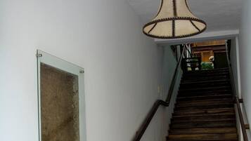 Una escalera de madera con barandilla, una lámpara colgante y un aviso en el pared.