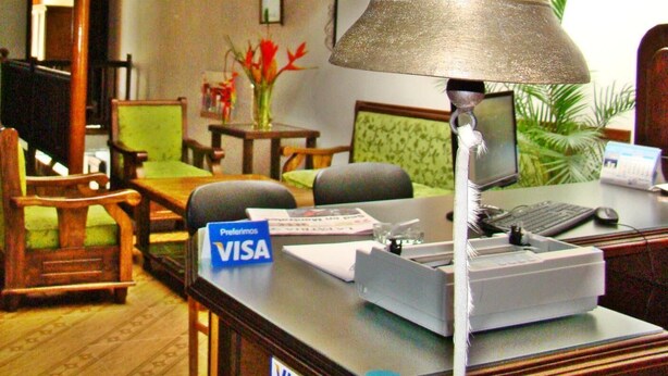 A reception desk with a 'Preferimos VISA' sign, a desktop computer, and a desk lamp. - Hospedaje Casa Real (Salamina)