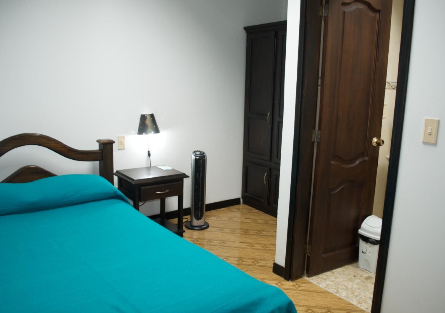 Un dormitorio con cama, mesita de noche, lámpara, calefactor, armario y puerta.