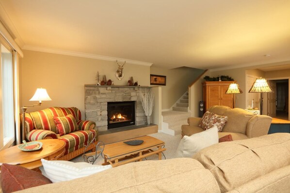 A cozy living room with a fireplace, striped sofa, and a staircase leading to another level.