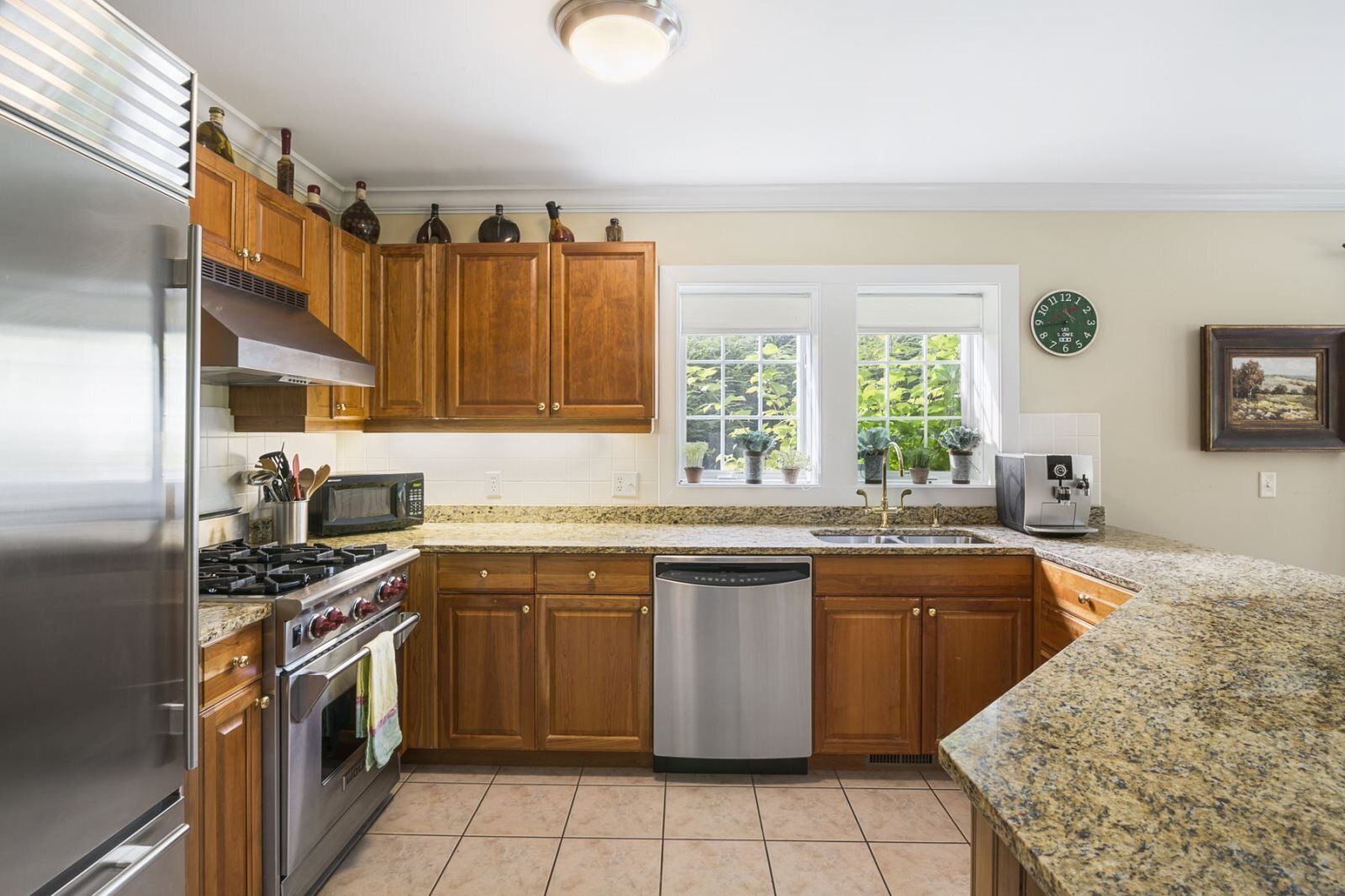 A modern kitchen with wooden cabinets, stainless steel appliances, granite countertops, and a window with plants.