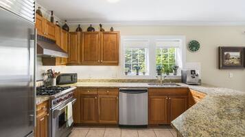 A modern kitchen with wooden cabinets, stainless steel appliances, granite countertops, and a window with plants.