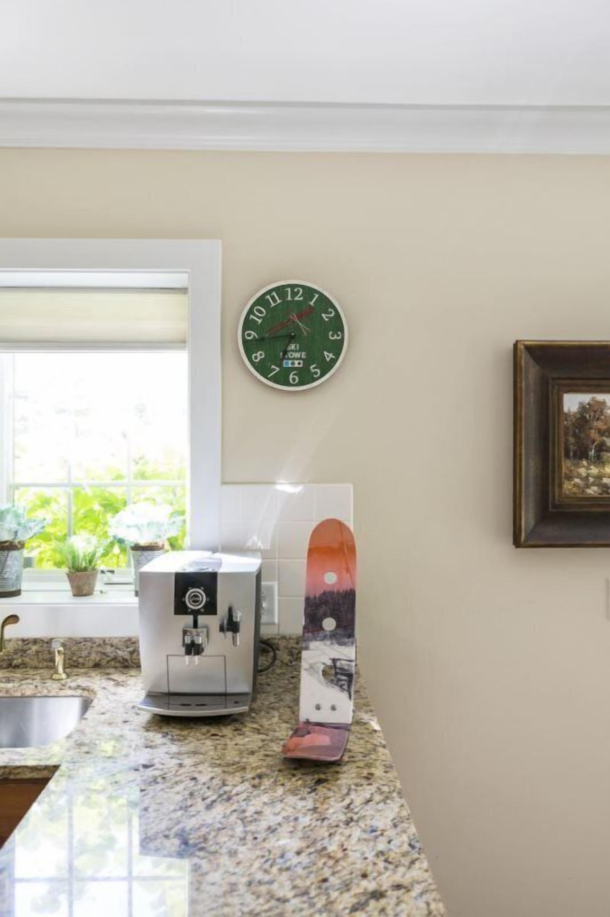 A kitchen with a coffee machine, a clock, and a framed picture on the wall.