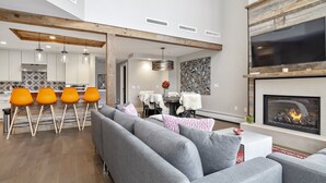 Ein modernes Wohnzimmer mit grauem Sofa, orangefarbenen Sesseln, einem Kamin und einer Küche im Hintergrund.