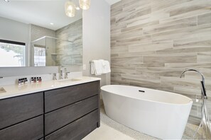 A modern bathroom with a freestanding bathtub, a vanity with dark wood drawers, and a large mirror. - 4BR Sterling Spruce Peak (Stowe)