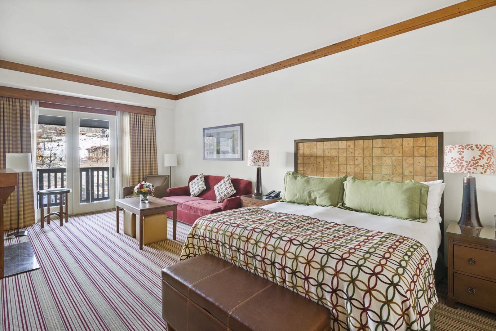 A hotel room with a bed, a sofa, a desk, and a balcony with curtains.