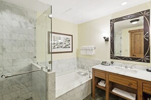A bathroom with a glass shower enclosure, a bathtub, a large mirror, and a wooden vanity with a marble countertop. - 1228/1230 Double Studio @ The Lodge at Spruce Peak (Stowe)