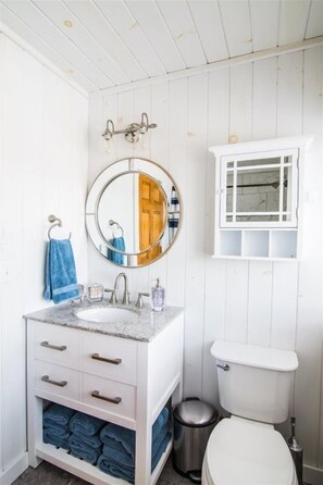 A bathroom with a white vanity, a round mirror, a sink, and a toilet. - Ayers Farm (Stowe)