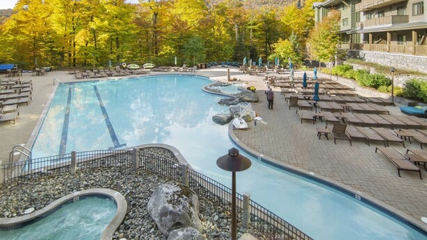 A swimming pool with lounge chairs and a hot tub, surrounded by trees and a mountain backdrop.