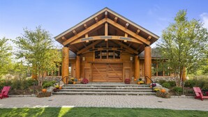 A log cabin with a large wooden entrance, stone steps, and a garden with autumn flowers.