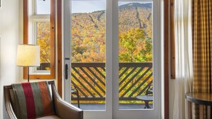 A room with a view of autumn foliage through a glass door, a chair with a striped cushion, and a lamp.