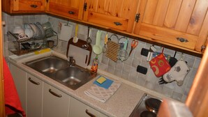 Une cuisine avec des meubles de rangement en bois, un évier en acier inoxydable et divers ustensiles de cuisine accrochés au mur.