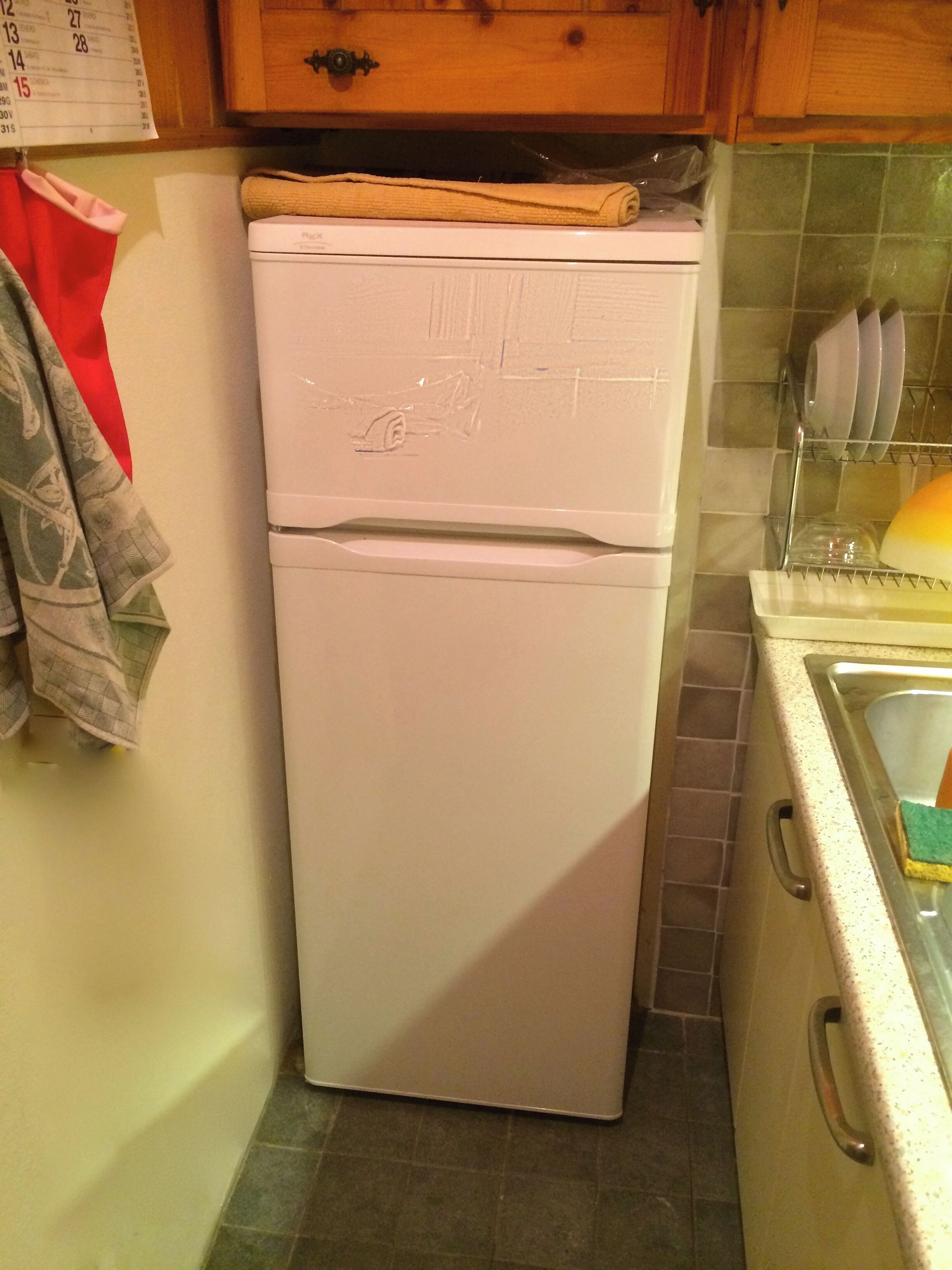 Una cocina con un refrigerador blanco, un mueble de madera, salpicadero de azulejos y un lavabo con escurreplatos.