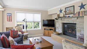 A living room with a stone fireplace, a television, a sofa, and a coffee table. - Americana at Topnotch Overlook (Stowe)