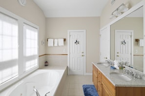A modern bathroom with a large bathtub, a vanity with a sink, and a mirror. There are two doors, one leading to a shower area and the other to a toilet.