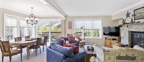 A spacious living room with a fireplace, a dining area with a table and chairs, and a large window offering a view of the outdoors.