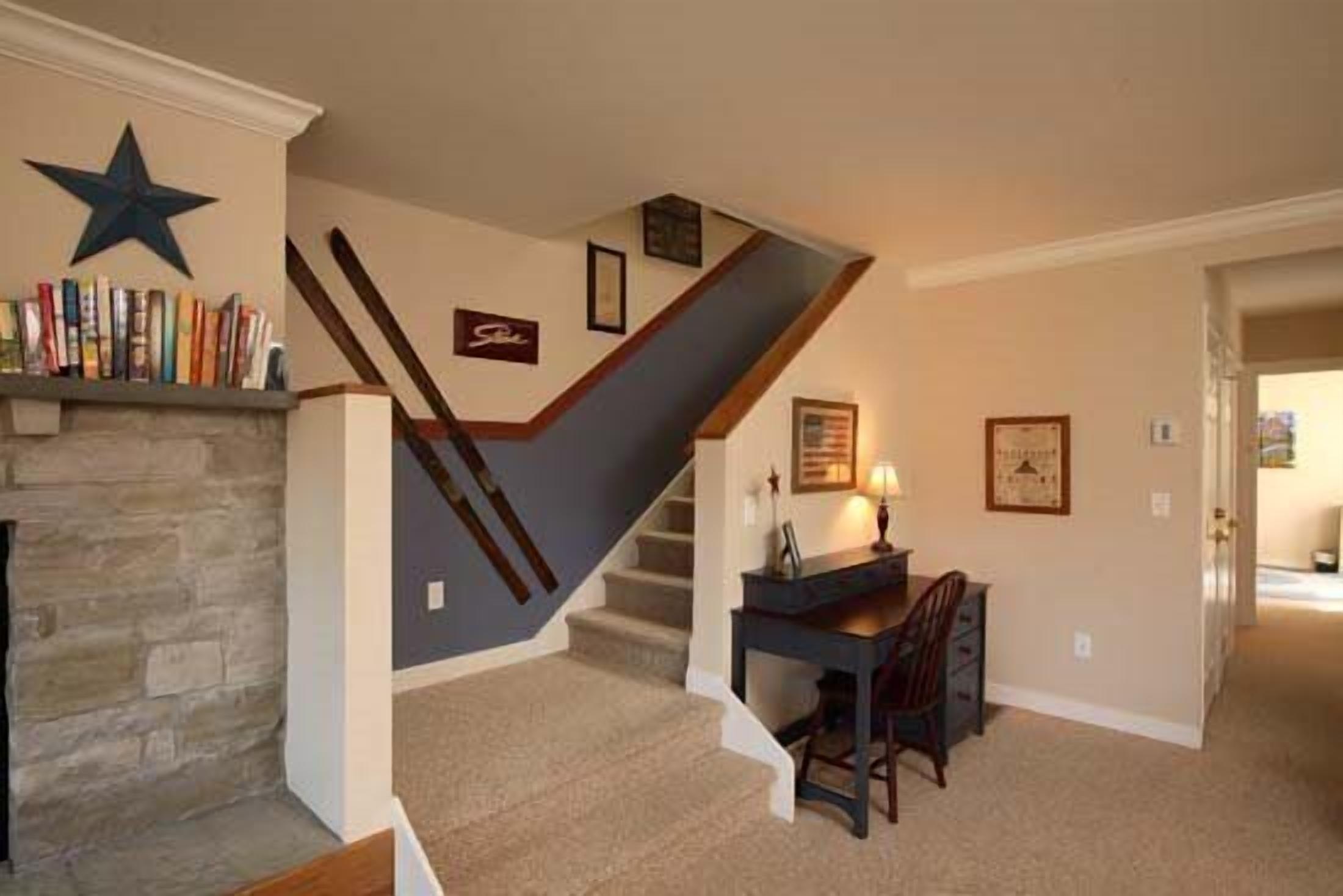 A staircase with a dark handrail and beige carpet, a desk with a chair, and a bookshelf with books.