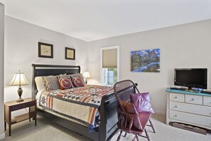 A neatly arranged bedroom with a bed, bedside lamps, a chair, a dresser, and a television.