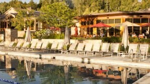 A pool area with lounge chairs and umbrellas, a building with outdoor seating, and a reflection in the water. - Americana at Topnotch Overlook (Stowe)