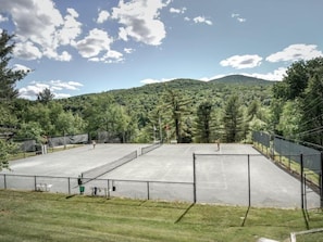 An outdoor tennis court surrounded by a fence, with a mountainous backdrop and trees. - 1BR Topnotch Condo (Stowe)