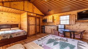 A cozy log cabin interior with a bed, a small kitchenette, a dining area, and a TV mounted on the wall. - Elite Cabins and RV Park (Big Spring)