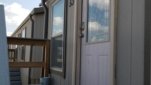 A single-story building with a beige exterior, a white door with a glass window, and a number '53' on the door. - Elite Cabins and RV Park (Big Spring)