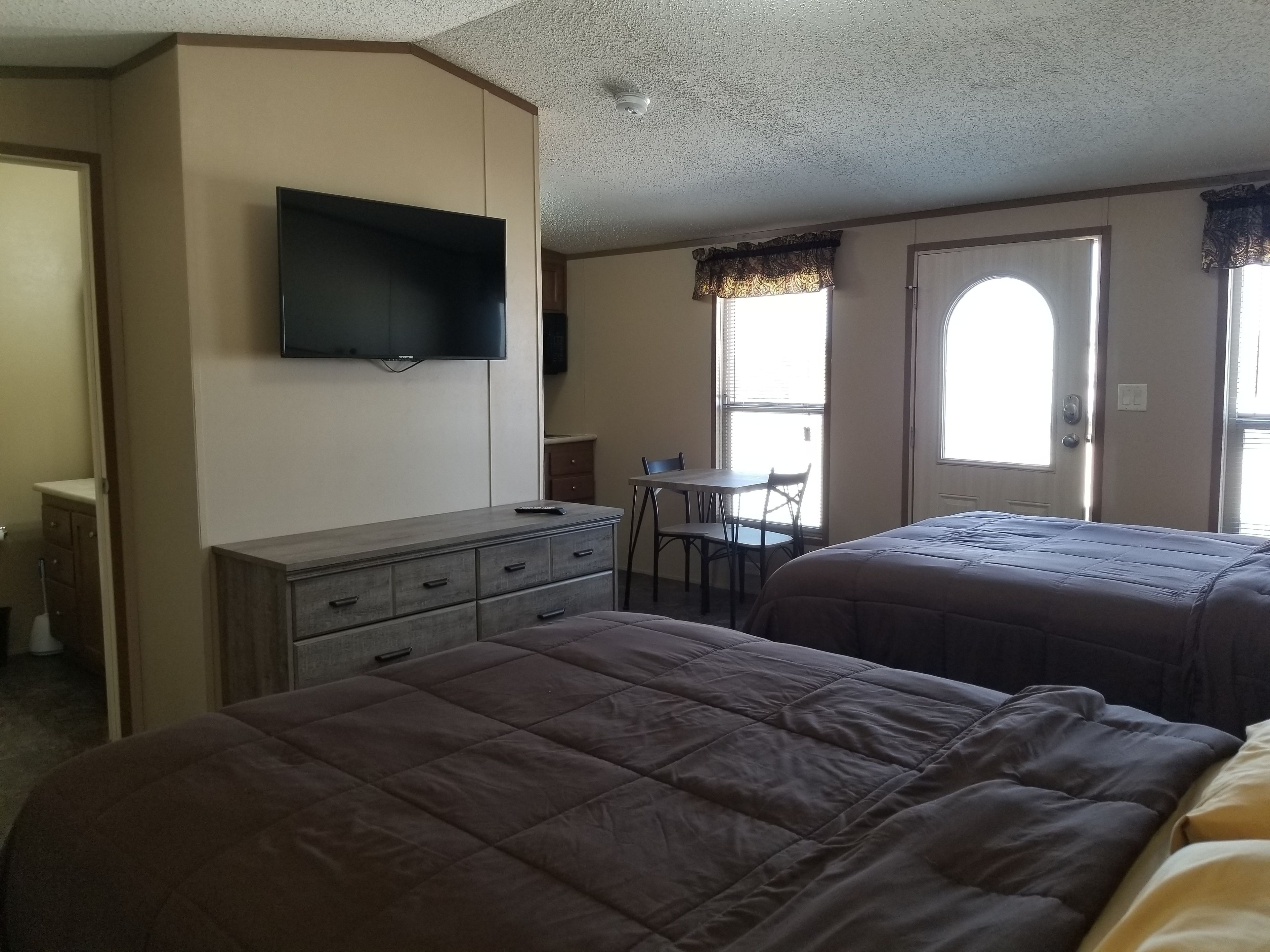 A hotel room with two beds, a TV mounted on the wall, a desk with a chair, and a window with curtains.