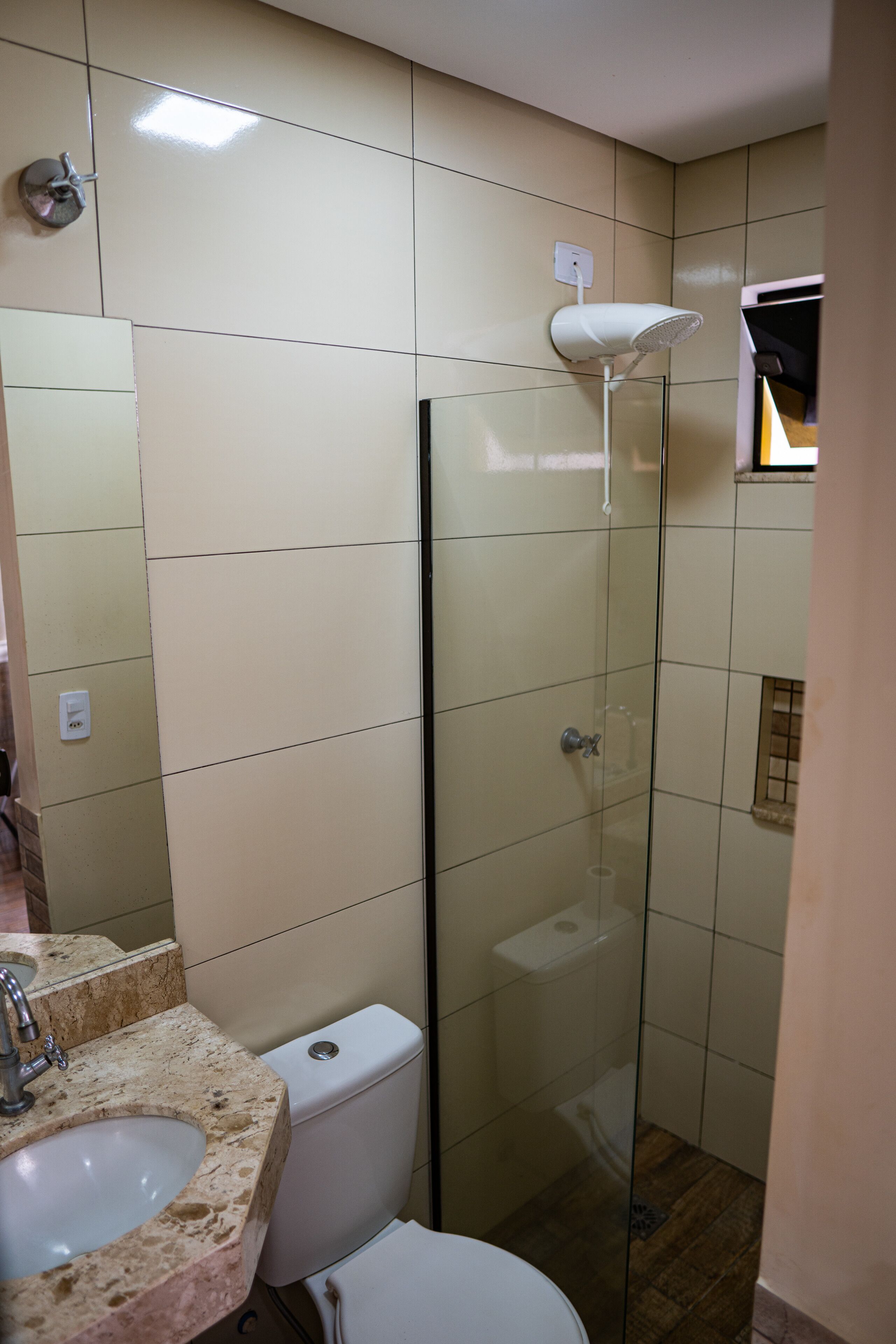 Un baño con ducha envuelta en vidrio, lavamanos con encimera de mármol y un inodoro.
