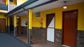 A hotel entrance with a yellow facade, a wooden door labeled '5', a fire extinguisher, and a covered walkway. - Hotel Nixon (Itai)