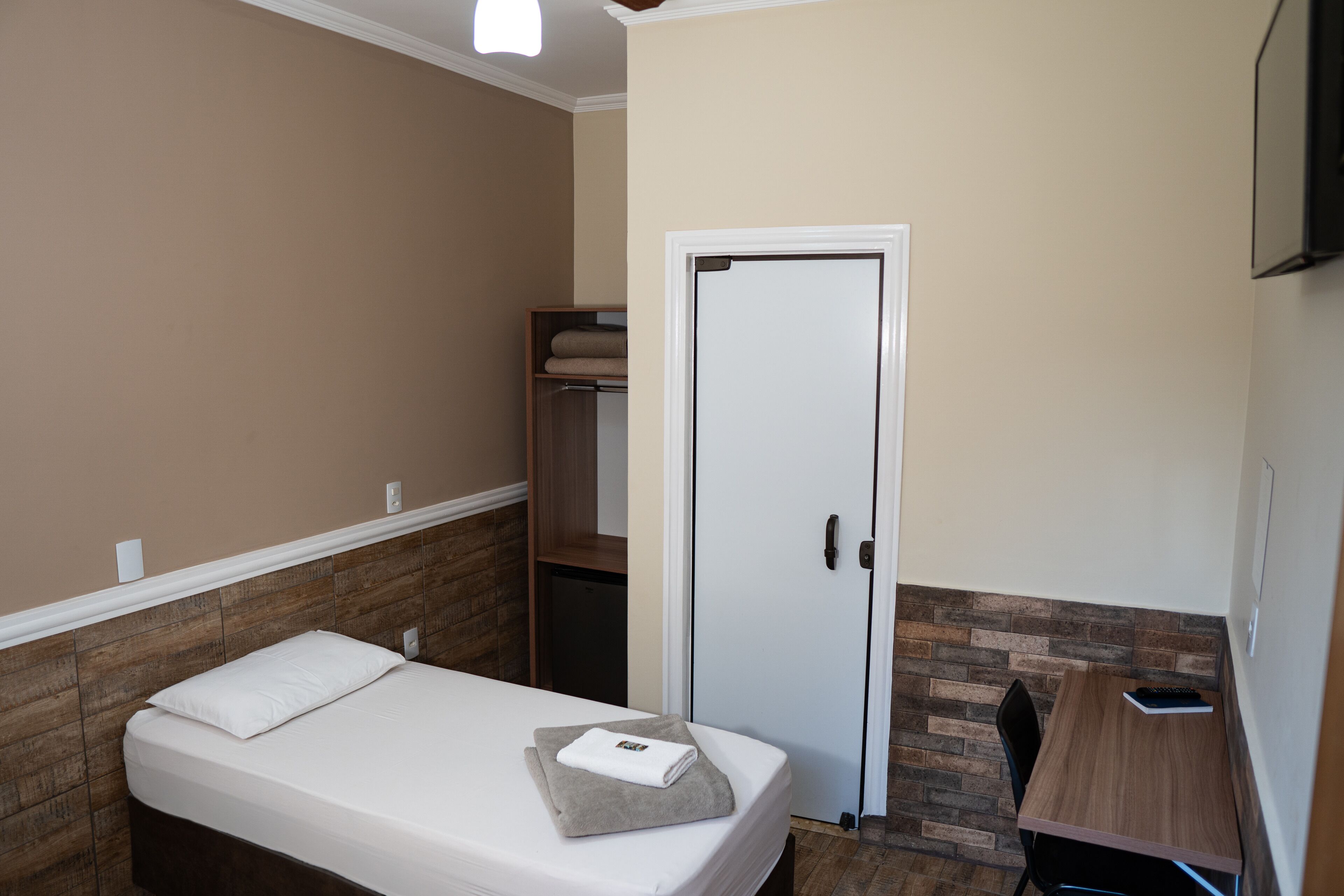 Une petite pièce, bien rangée, avec un lit simple, un bureau et une armoire.