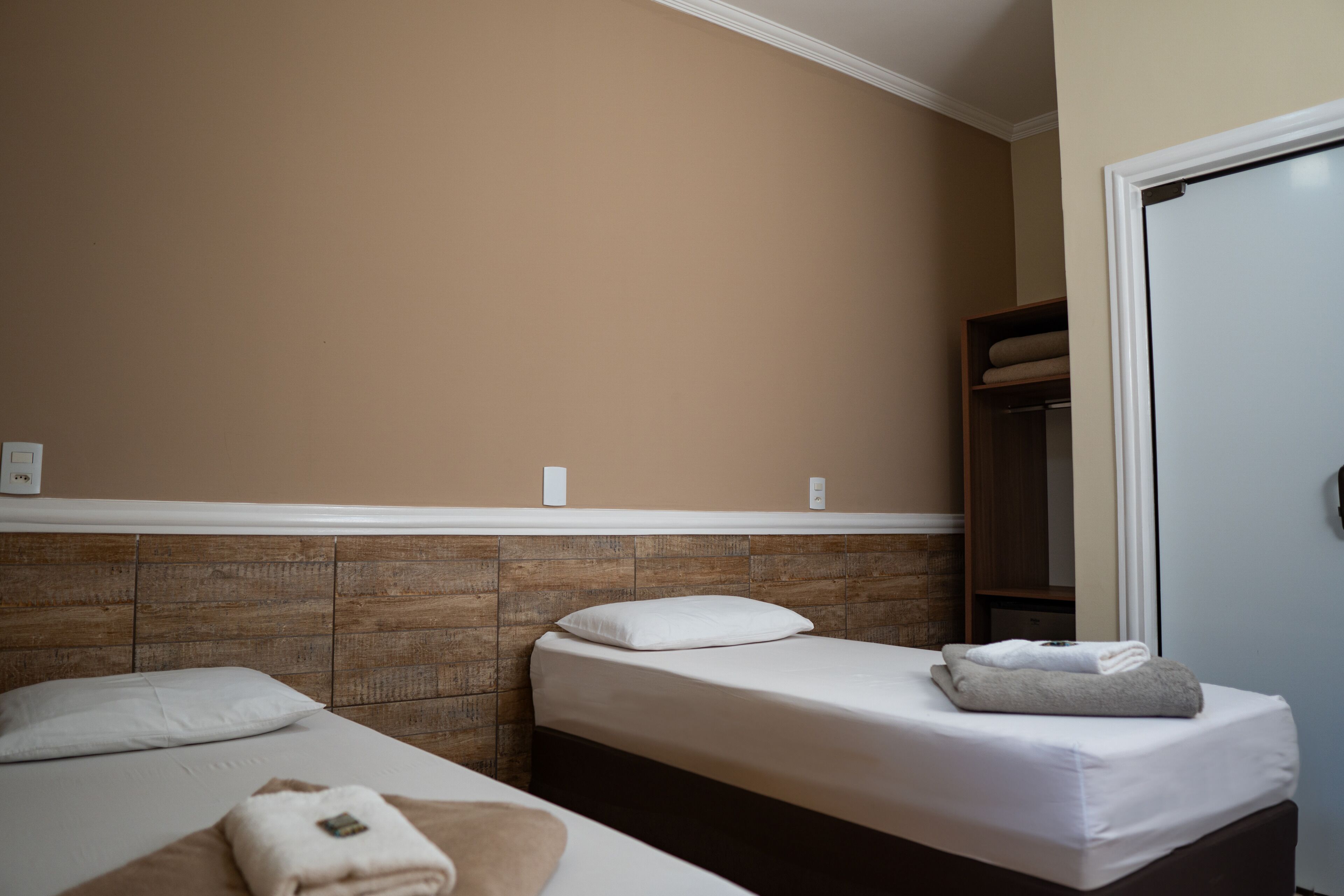 A hotel room with two beds, a wooden headboard, a closet, and a door.
