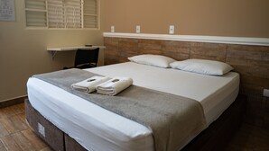 A neatly made bed with two pillows and two folded towels, a small desk with a chair, and a window with blinds. - Hotel Nixon (Itai)