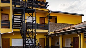 A multi-story building with a central staircase, multiple doors, and a small attached structure with a tiled roof. - Hotel Nixon (Itai)