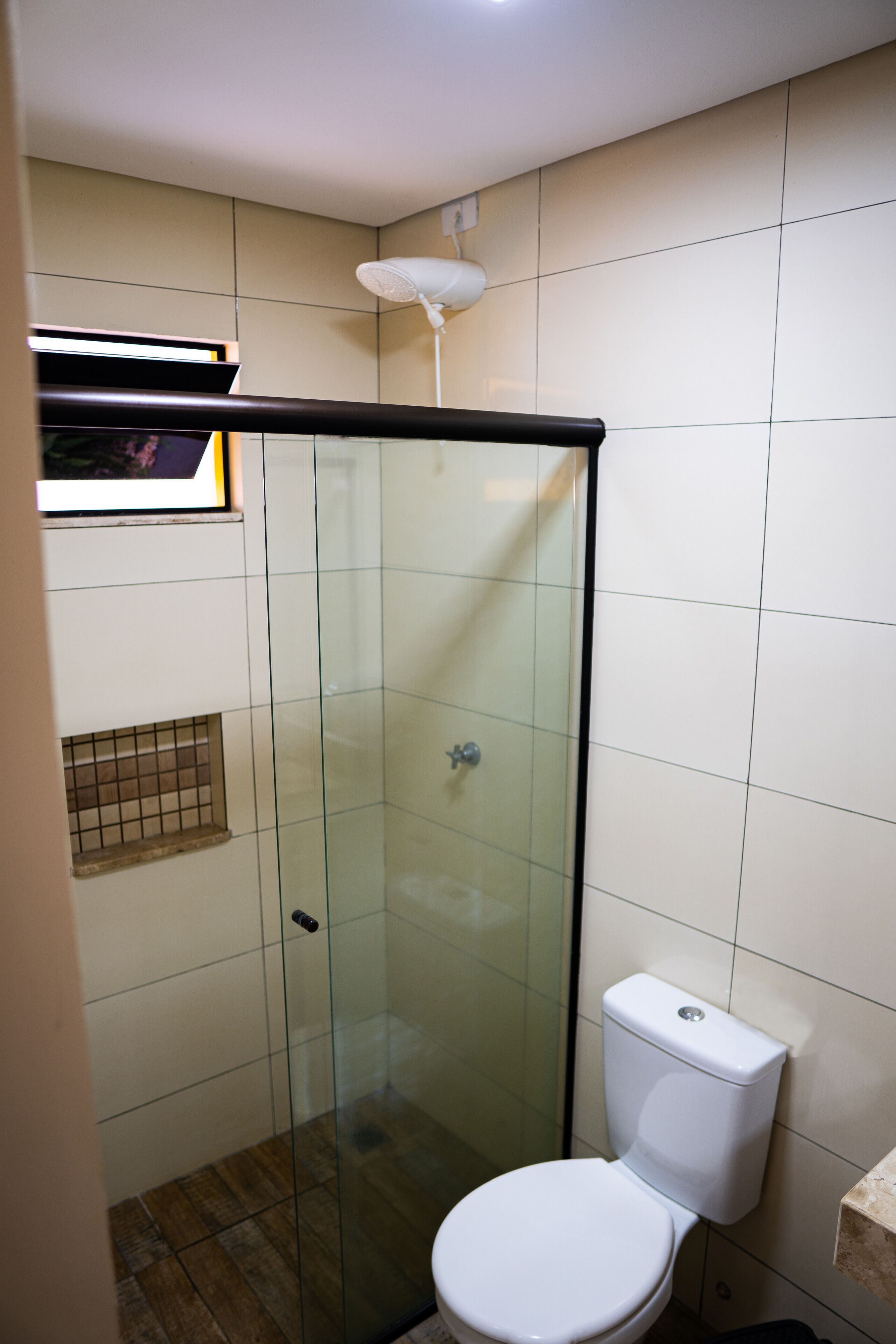 A bathroom with a glass-enclosed shower, a white toilet, and a small shelf above the toilet.