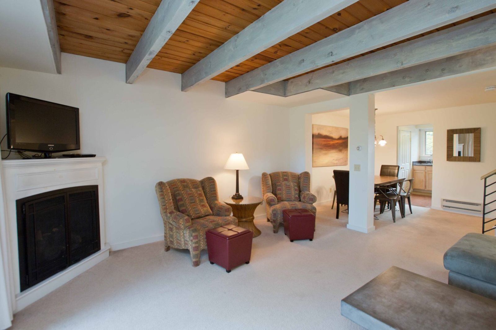 A living room with a fireplace, two patterned armchairs, a small table with a lamp, and a television on a mantel.