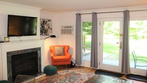A living room with a fireplace, a television, a chair, and a door leading outside. - Topnotch_463 (Stowe)