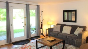 A living room with a grey sofa, a coffee table, a lamp, and a coat rack. - Topnotch_463 (Stowe)