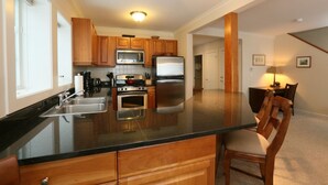 A modern kitchen with wooden cabinets, stainless steel appliances, a large island, and a dining area with a table and chairs. - 3BR Overlook at Topnotch (Stowe)