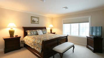 A bedroom with a bed, two bedside tables with lamps, a bench, a dresser, a television, and a window with blinds.