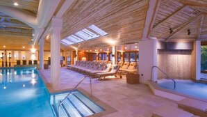 An indoor swimming pool with lounge chairs and a sunbed area, surrounded by wooden beams and large windows. - 3BR Overlook at Topnotch (Stowe)
