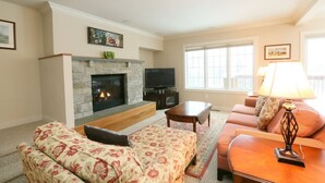 A living room with a fireplace, sofa, television, and a lamp. - 3BR Overlook at Topnotch (Stowe)