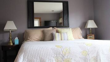 A neatly made bed with a leaf-patterned quilt, two bedside lamps, and a large mirror above the bed.
