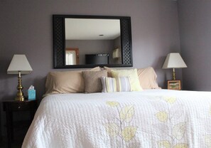 Una cama bien hecha con colcha de diseño floral, dos lámparas de noche y un espejo grande sobre la cama.
