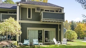 A two-story house with a balcony, a lawn with chairs, and trees in the background. - Brookside 2 BR at Topnotch (Stowe)