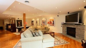 A spacious living room with a large sectional sofa, a fireplace, and a flat-screen TV mounted above it. - 627a_topnotch (Stowe)