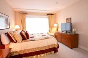A bedroom with a large bed, a dresser, a television, and a window with curtains. - 627a_topnotch (Stowe)